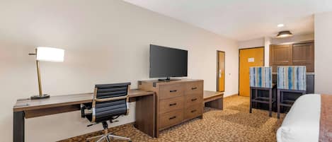 A hotel room with a desk, chair, television, dresser, and two armchairs.