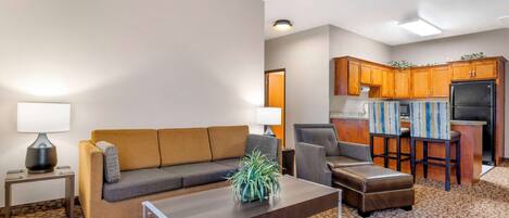 Una sala de estar con sofá, una mesa de centro y una cocina con armarios de madera y refrigerador.