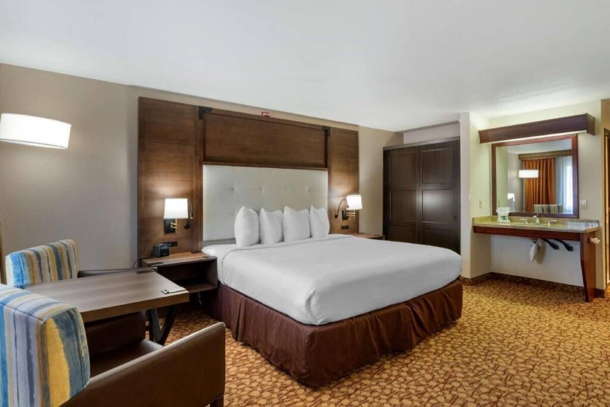 A hotel room with a large bed, a desk, a chair, a mirror, and a bathroom.