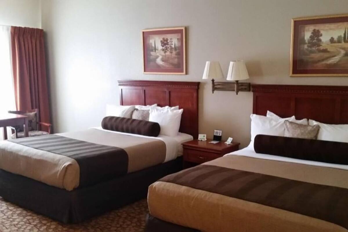 Two double beds with headboards, bedside tables, lamps, and framed pictures on the wall.