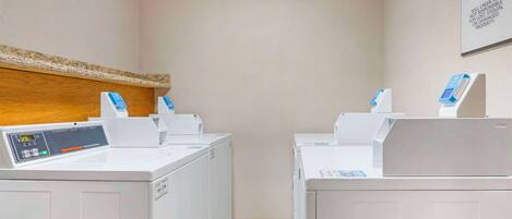 A laundry room with two front-loading washers and dryers, a control panel, and a wooden headboard on the wall.