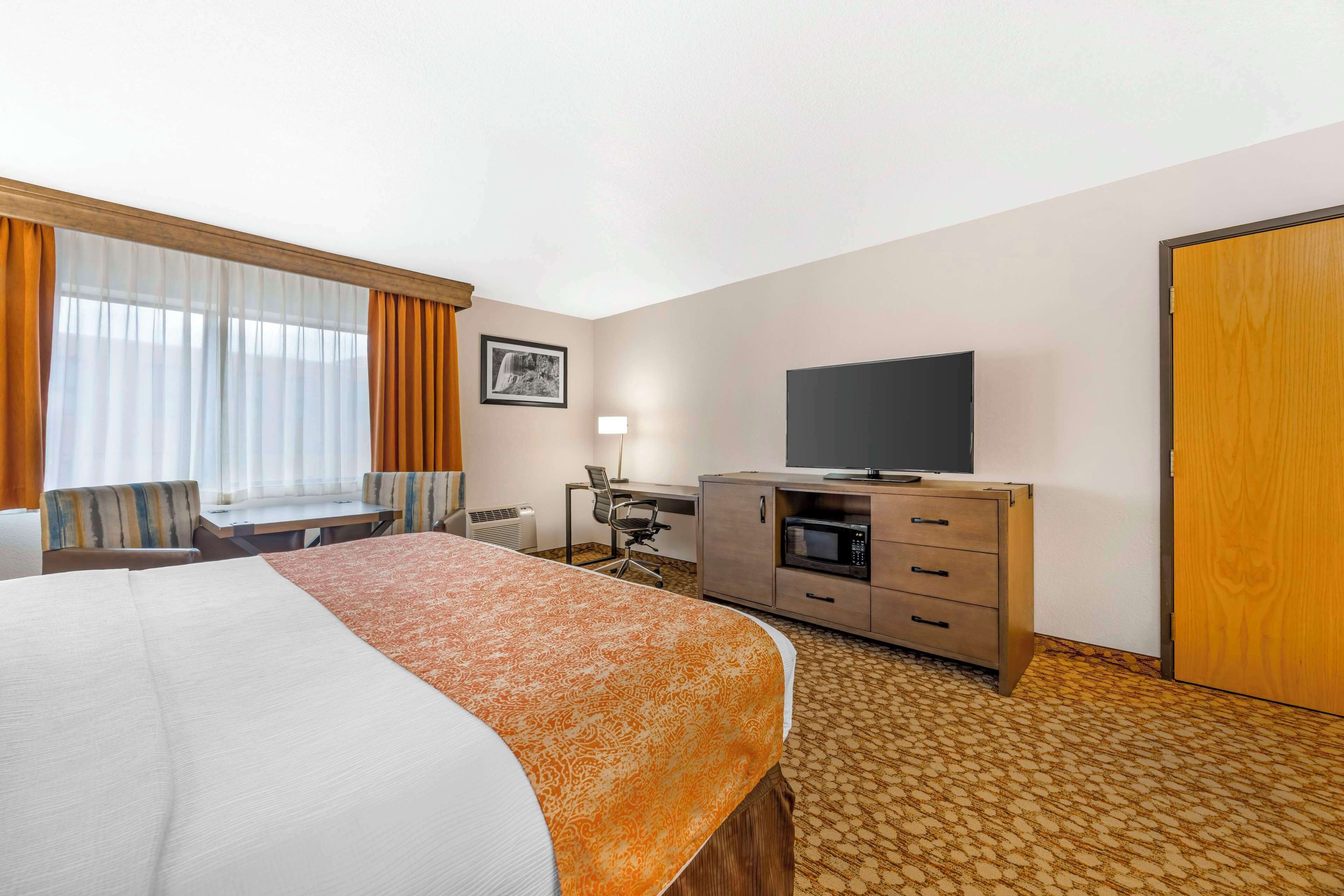 Una habitación de hotel con una cama grande, un escritorio, televisión, microondas y armario.