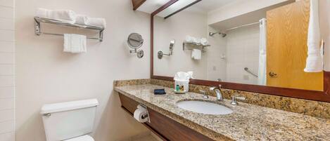 A bathroom with a toilet, sink, and mirror. There are towels on a shelf and a towel rack.