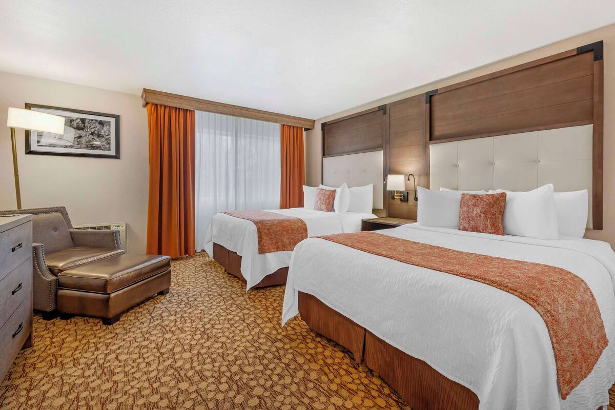 A hotel room with two beds, a desk, a chair, and a patterned carpet.