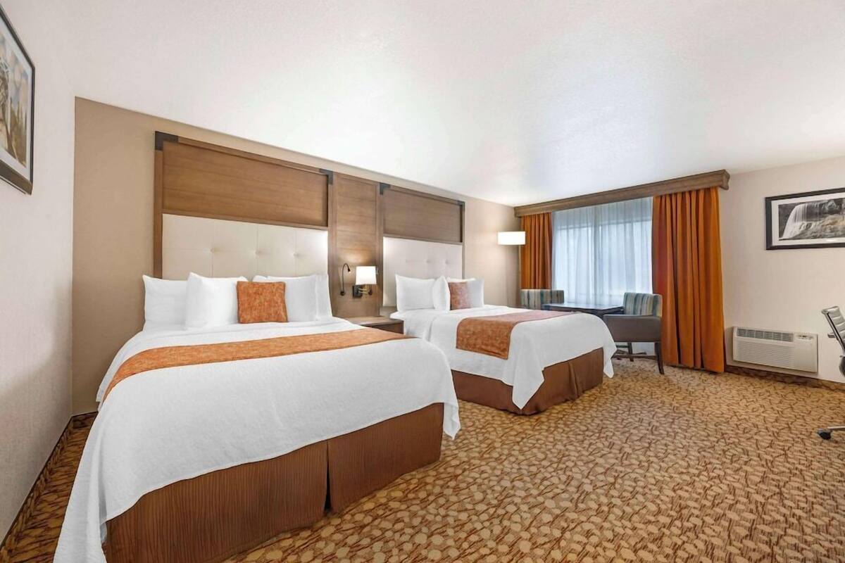A hotel room with two beds, a desk, and a large window with curtains.