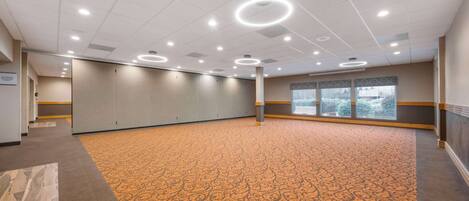 Une salle de conférence dotée d’un tapis à motifs, de luminaires encastrés et d’une grande fenêtre avec des stores.
