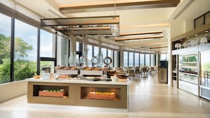A modern hotel lobby with a central buffet area, large windows, and a view of greenery. - Hotel Nikko Guam (Tamuning)