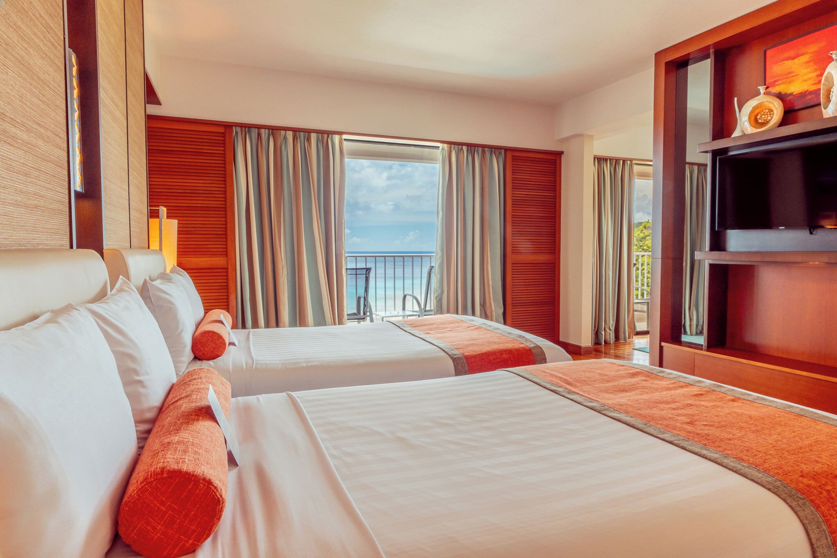 A hotel room with two beds, a balcony with a view, and a television on a wooden shelf.