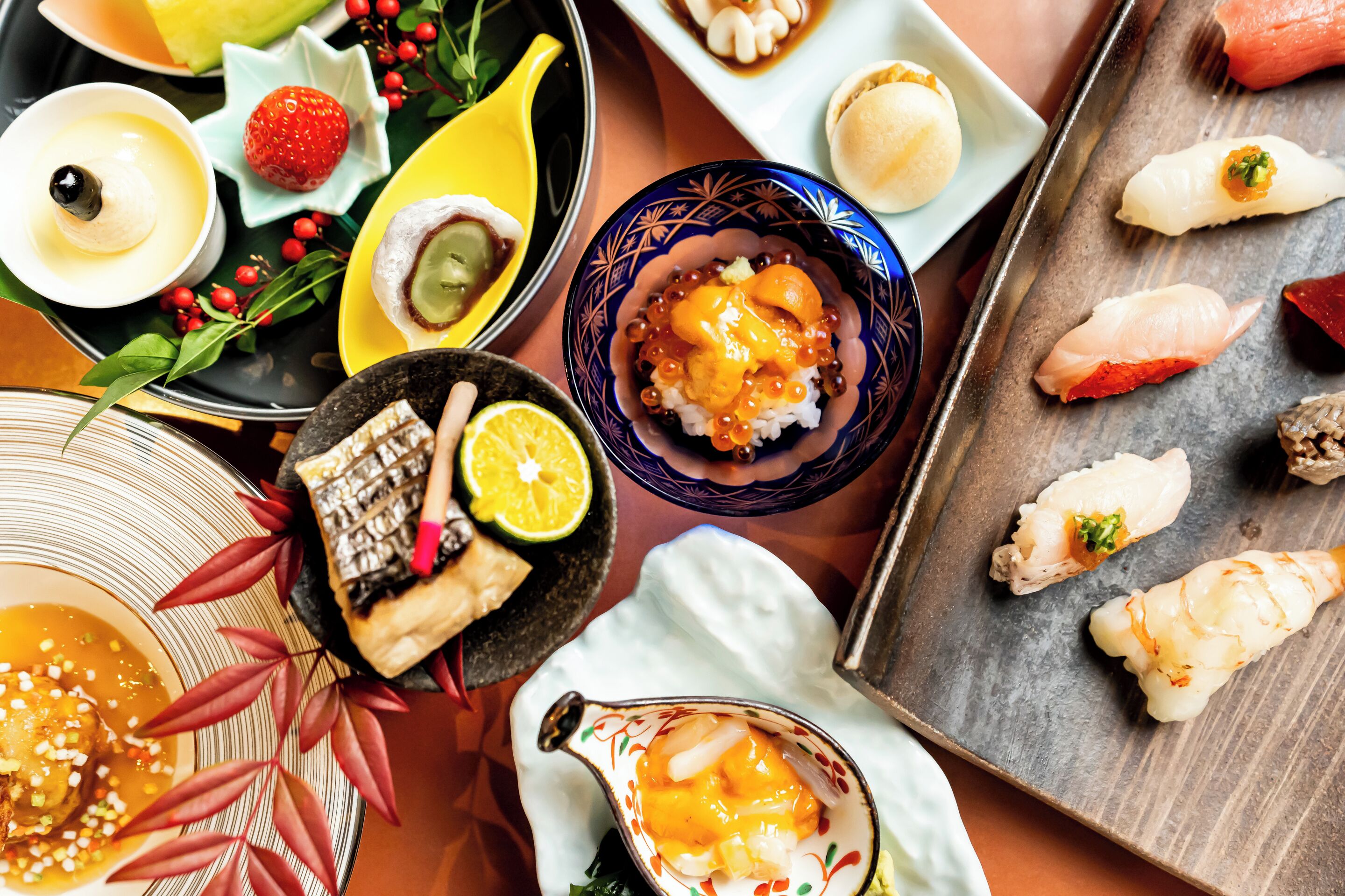 A variety of Japanese dishes including sushi, sashimi, and rice bowls, arranged on a table with a variety of colorful plates and bowls.