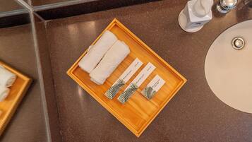 A wooden tray with two white towels and three cards with palm tree designs, placed on a bathroom counter next to a sink and a mirror.