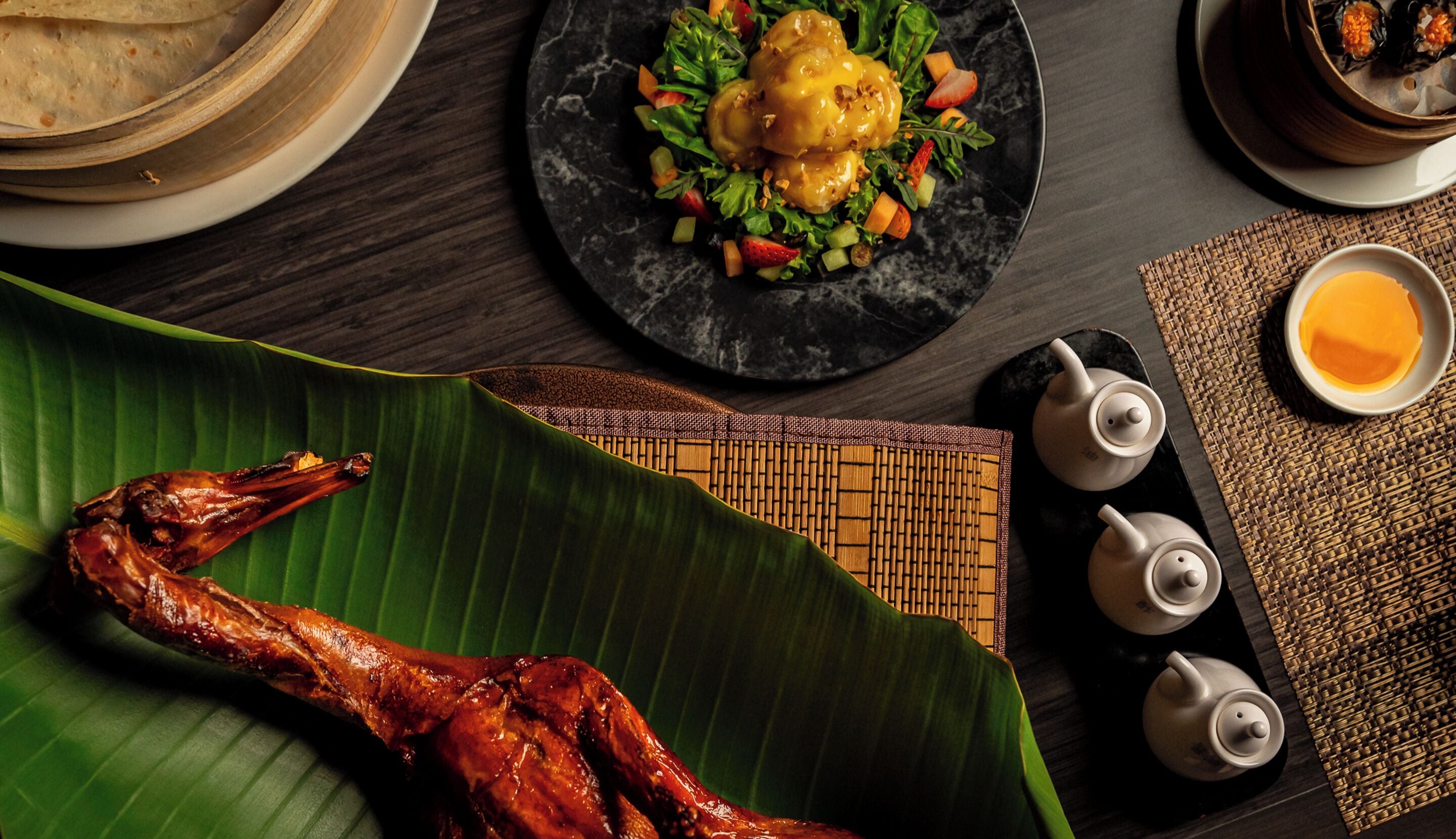 A dining table with a roasted chicken, a plate of food, and a teapot set.