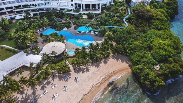 An aerial view of a resort with multiple swimming pools, a beach, and lush greenery. - Hotel Nikko Guam (Tamuning)