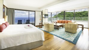A hotel room with a large bed, a balcony with a view of the sea, and a seating area with wicker furniture. - Hotel Nikko Guam (Tamuning)