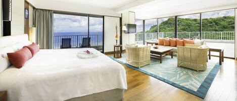 Habitación de hotel con una cama grande, un balcón con vistas al mar y una zona de estar con mobiliario de mimbre.