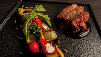 A steak with a dark sauce on a black plate, accompanied by a colorful vegetable dish.