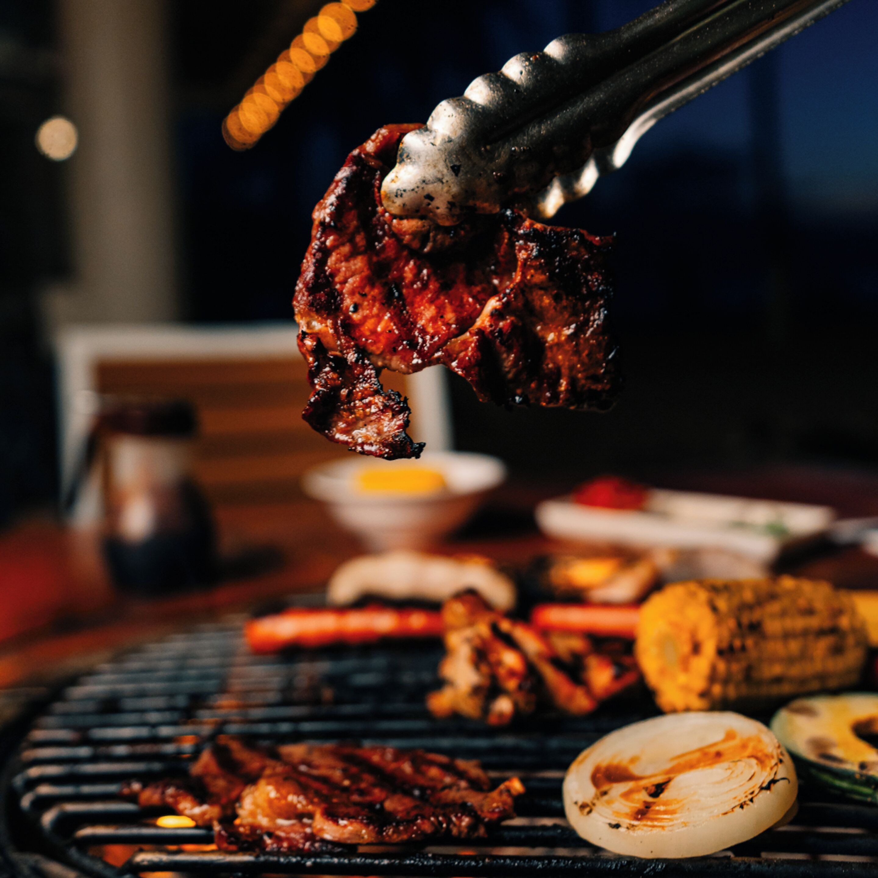 A close-up of grilled meat being held by tongs over a grill.