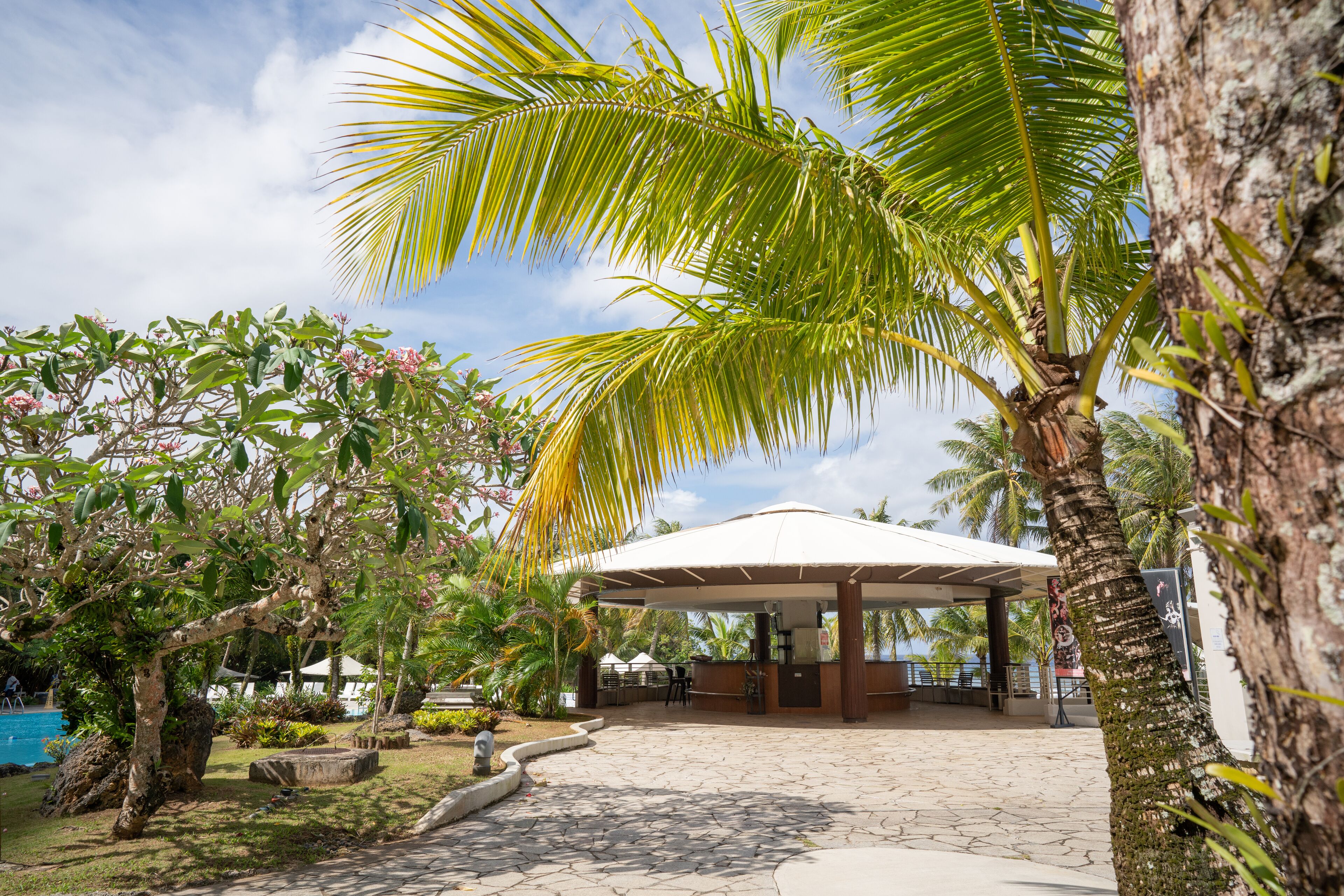 A covered outdoor area with a pool, palm trees, and a gazebo.
