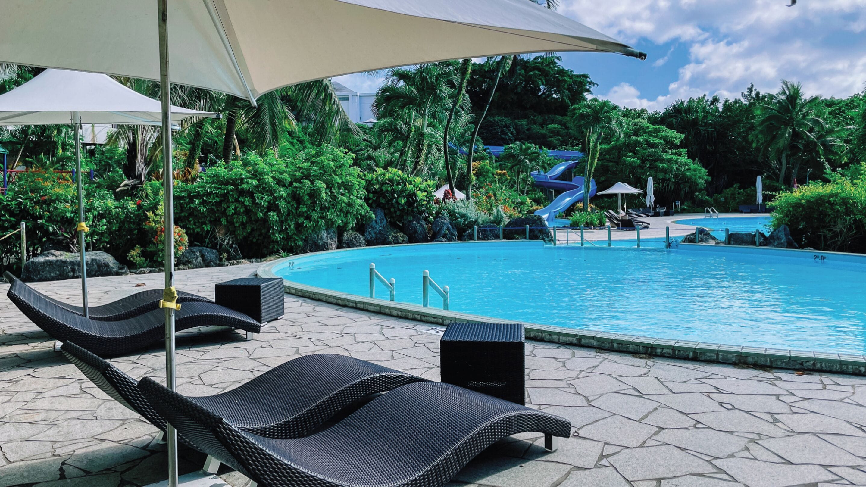A swimming pool with lounge chairs and umbrellas, surrounded by lush greenery.