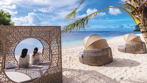 A beach setting with a circular viewing area, two wicker lounge chairs, and a palm tree. - Hotel Nikko Guam (Tamuning)