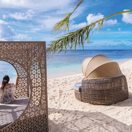 A beach setting with a circular viewing area, two wicker lounge chairs, and a palm tree.