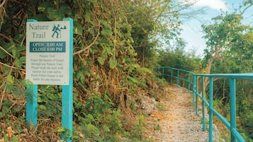 A nature trail sign with opening and closing times, caution for safety, and a disclaimer about hotel liability.