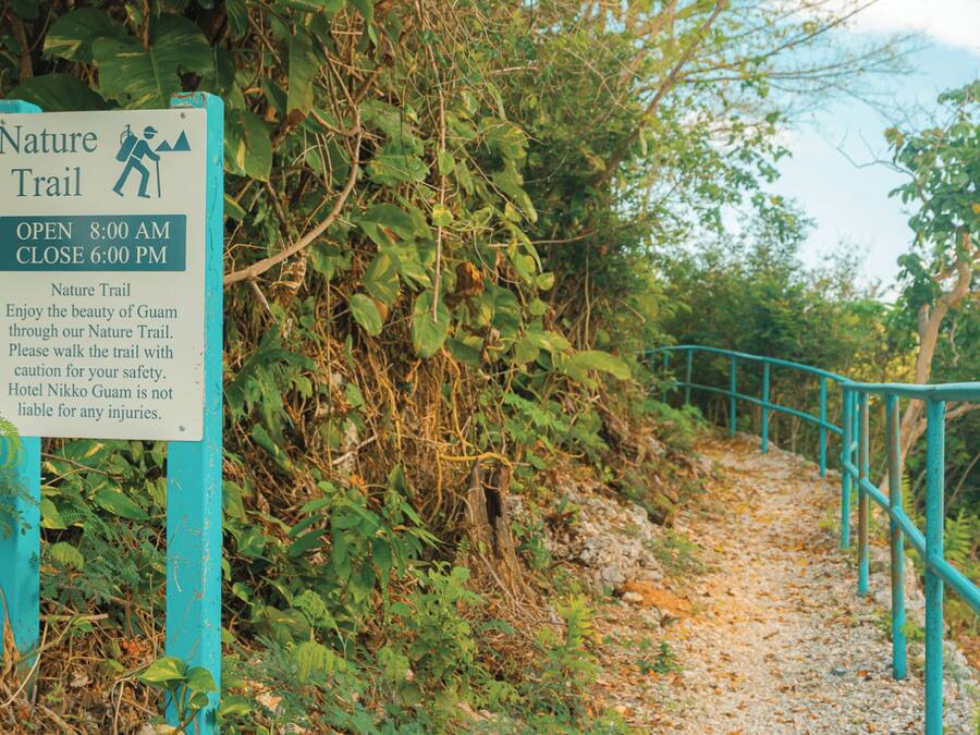 A nature trail sign with opening and closing times, caution for safety, and a disclaimer about hotel liability.