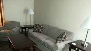 A living room with a grey sofa, two armchairs, a coffee table, and two side tables with lamps. - Rodeway Inn Little Falls (Little Falls)