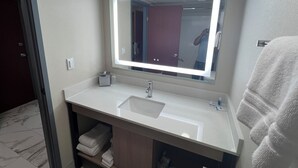 A bathroom with a large mirror, white sink, and a towel rack. - Rodeway Inn Little Falls (Little Falls)