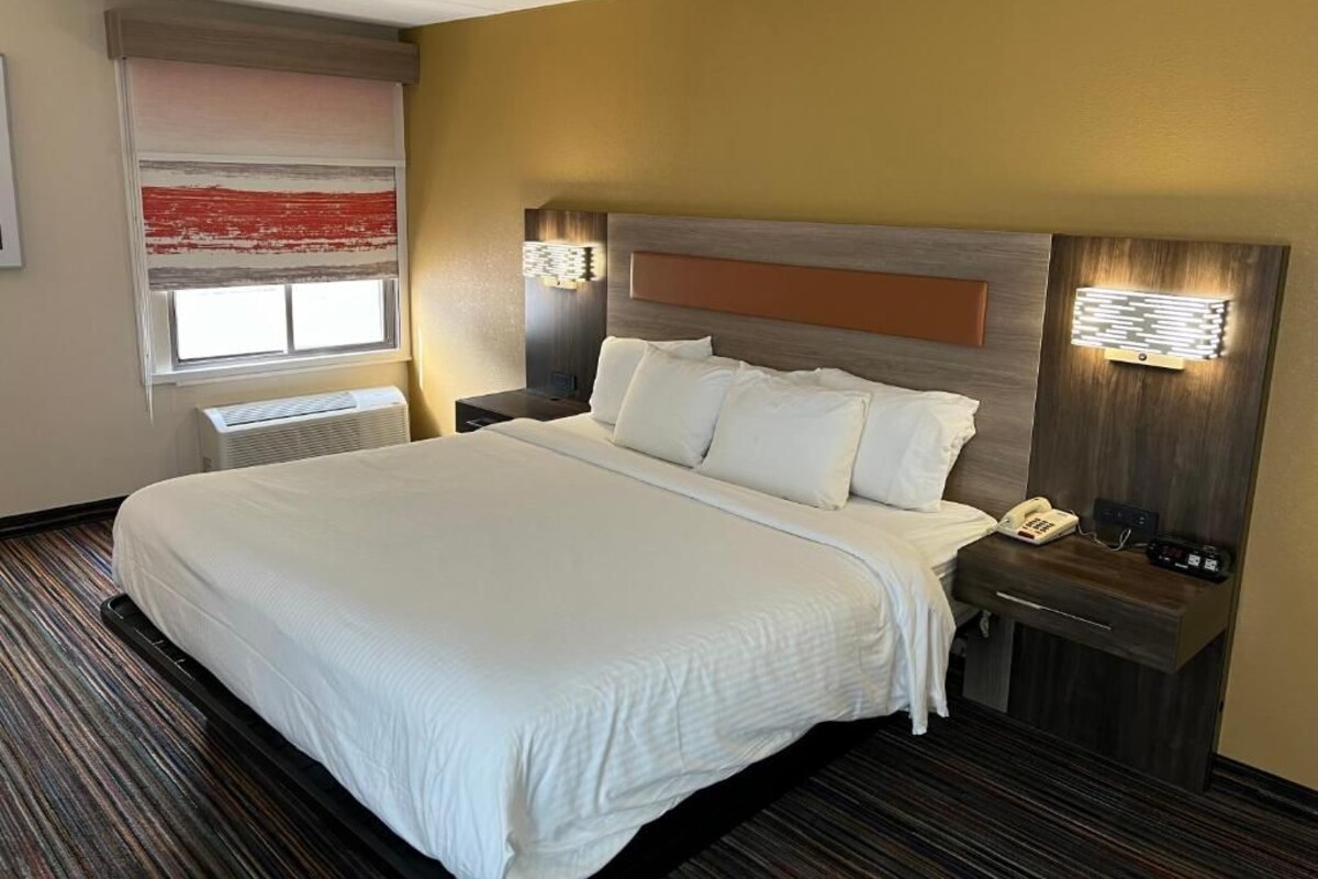 Ein Hotelzimmer mit einem großen Bett, einem Nachttisch mit Telefon und einer an der Wand befestigten Lampe.