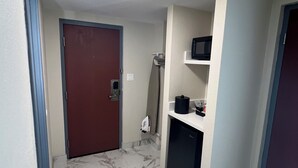 A hallway with a marble floor, a red door, a microwave, and a small refrigerator.