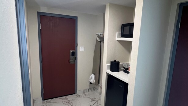 A hallway with a marble floor, a red door, a microwave, and a small refrigerator. - Rodeway Inn Little Falls (Little Falls)