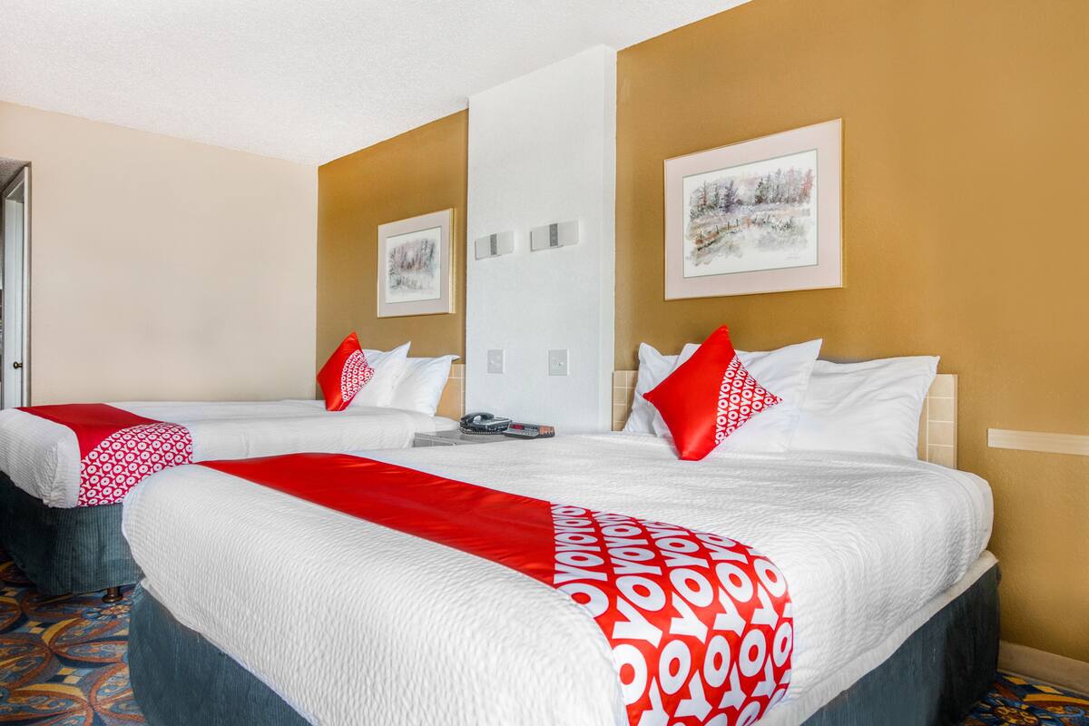 A hotel room with two beds, a red and white patterned bedspread, a framed picture on the wall, and a patterned carpet.