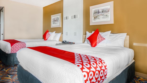 Une chambre d’hôtel avec deux lits, une couvre-lit rouge et blanche à motifs, un tableau encadré au mur et une moquette à motifs.