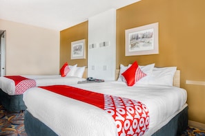 A hotel room with two beds, a red and white patterned bedspread, a framed picture on the wall, and a patterned carpet. - OYO Hotel Wichita Falls - Downtown (Wichita Falls)
