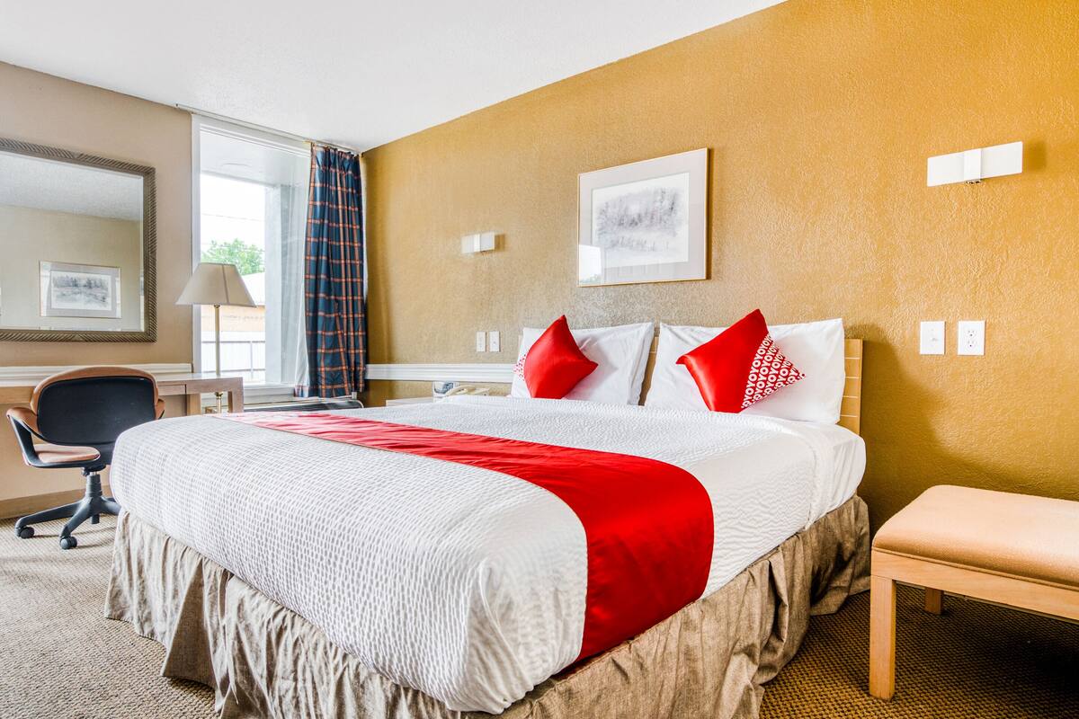 A hotel room with a large bed, a desk, a chair, and a window with curtains.