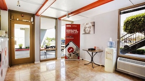 Un hall d’hôtel avec un sol carrelé, un comptoir d’accueil, un distributeur d’eau et une affiche faisant la promotion de l’application OYO.