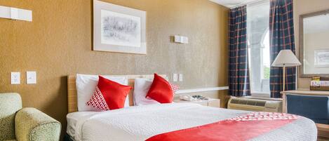 A hotel room with a large bed, a desk, a chair, and a window with curtains.