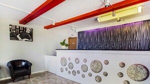 Un espace d’accueil au design moderne, comprenant un comptoir de réception, un fauteuil en cuir noir, une plante fixée au mur et un mur décoré d’un motif.
