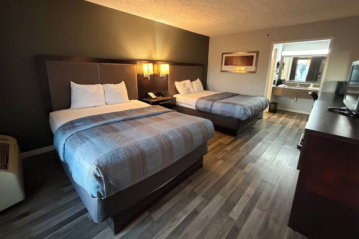 A hotel room with two beds, a desk, a chair, and a bathroom visible through an open door.