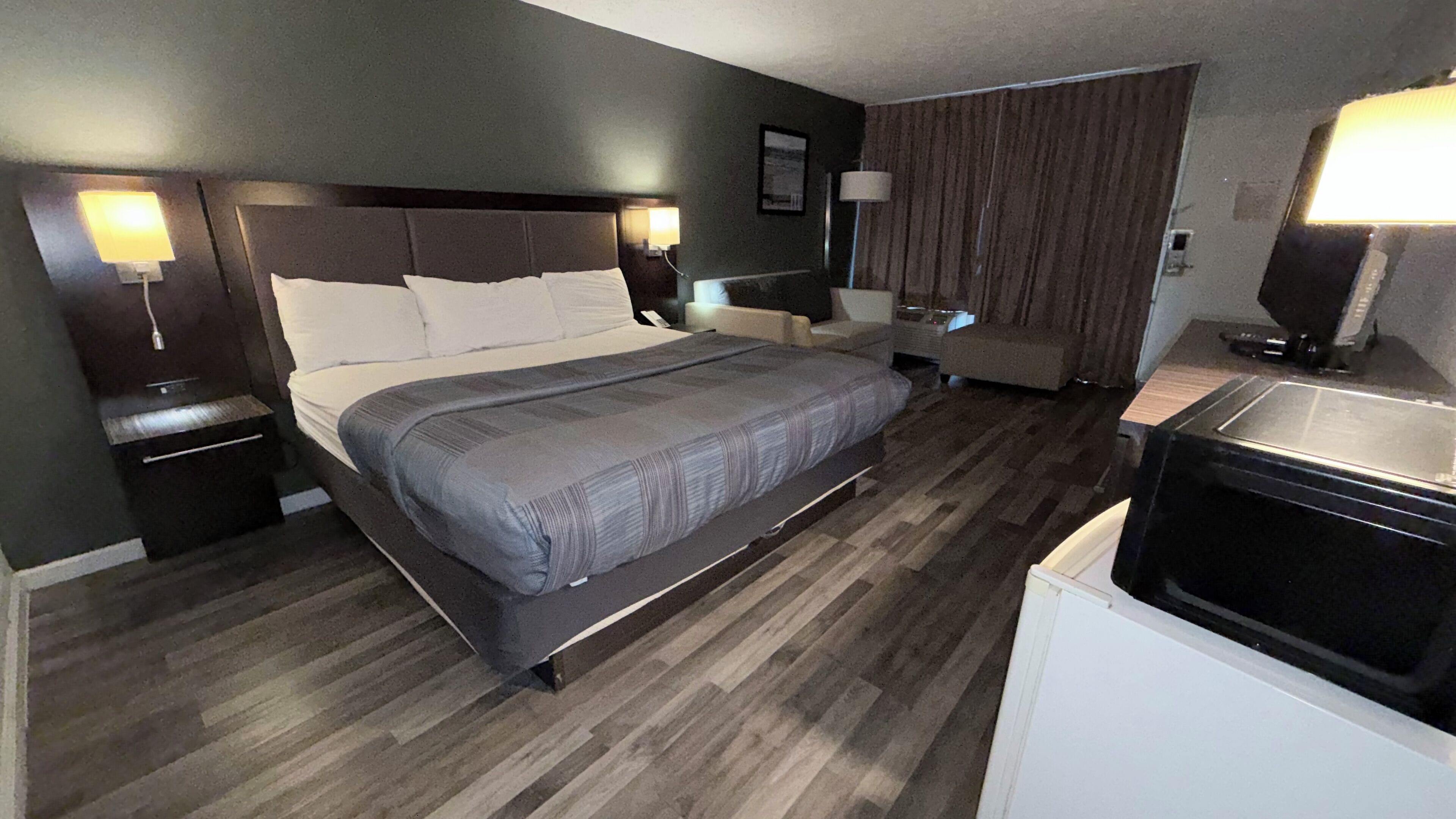 A hotel room with a large bed, a desk, a chair, a TV, and a minibar.