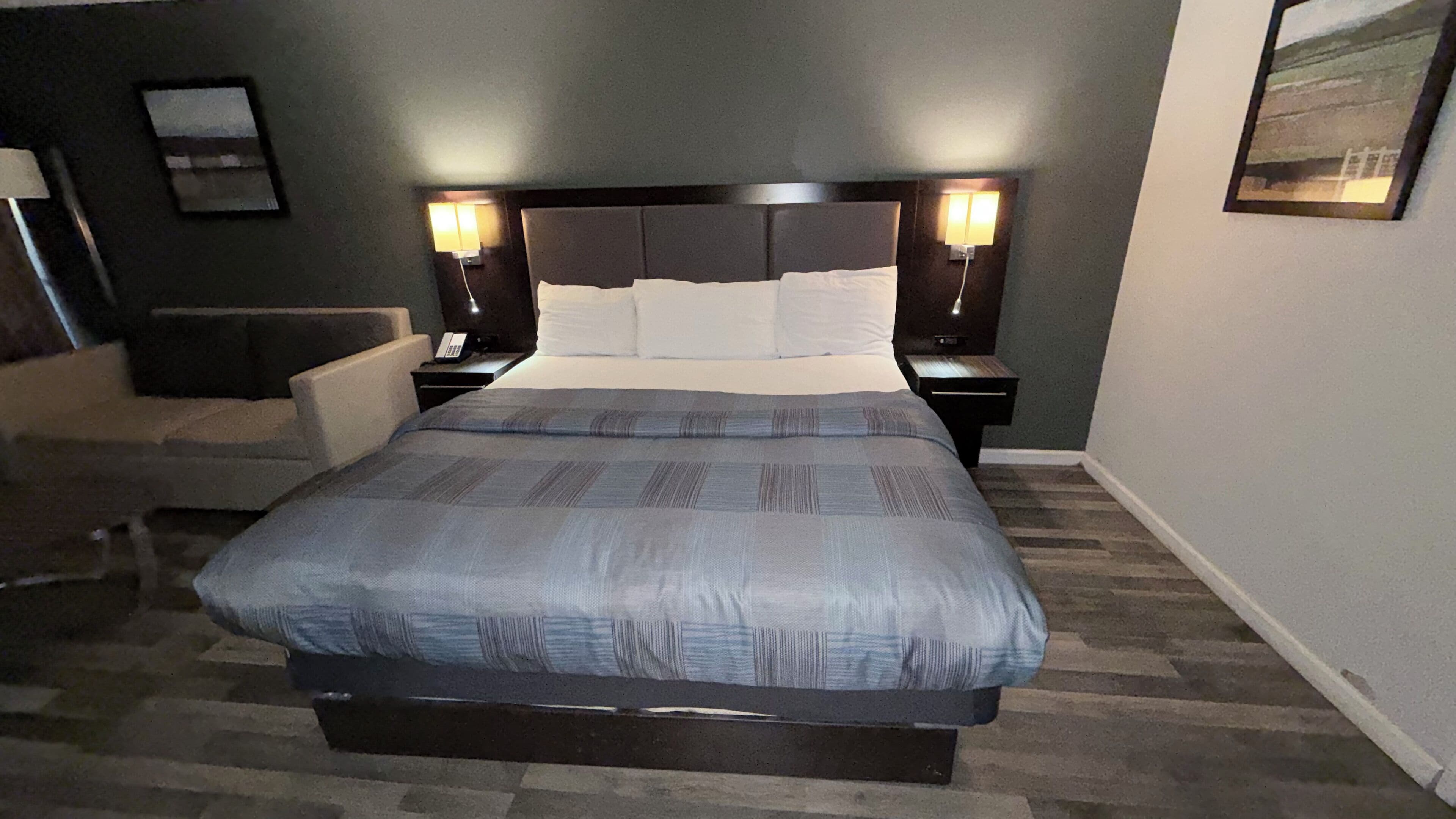 A neatly arranged bedroom with a large bed, two bedside tables with lamps, a chair, and a small desk with a telephone.