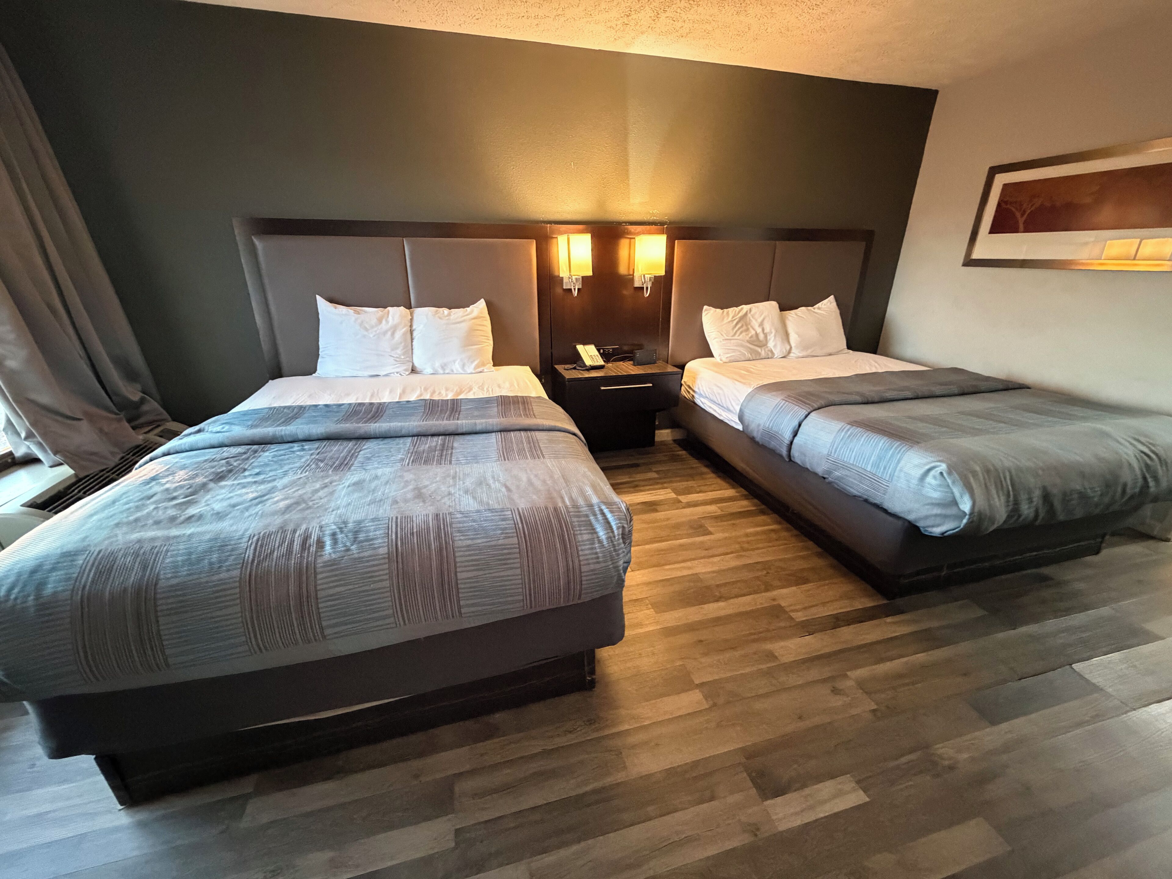 A hotel room with two beds, a nightstand with a lamp, and a painting on the wall.