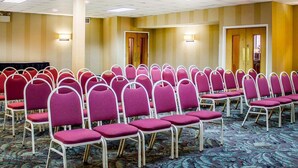 Ein Konferenzraum mit Reihen von Stühlen, Teppichboden und einer Projektionsleinwand.