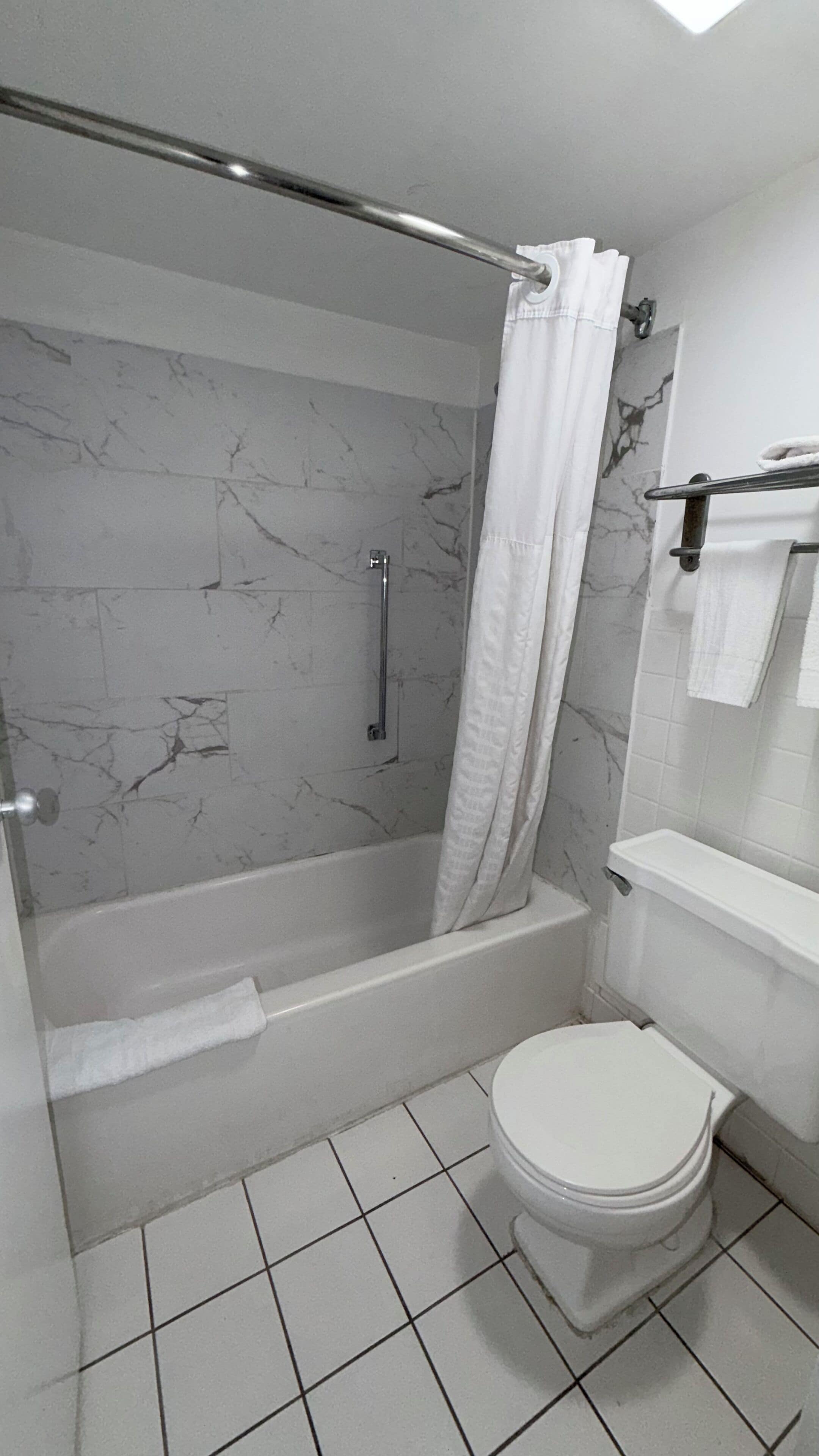 A bathroom with a shower, toilet, and marble-tiled walls.