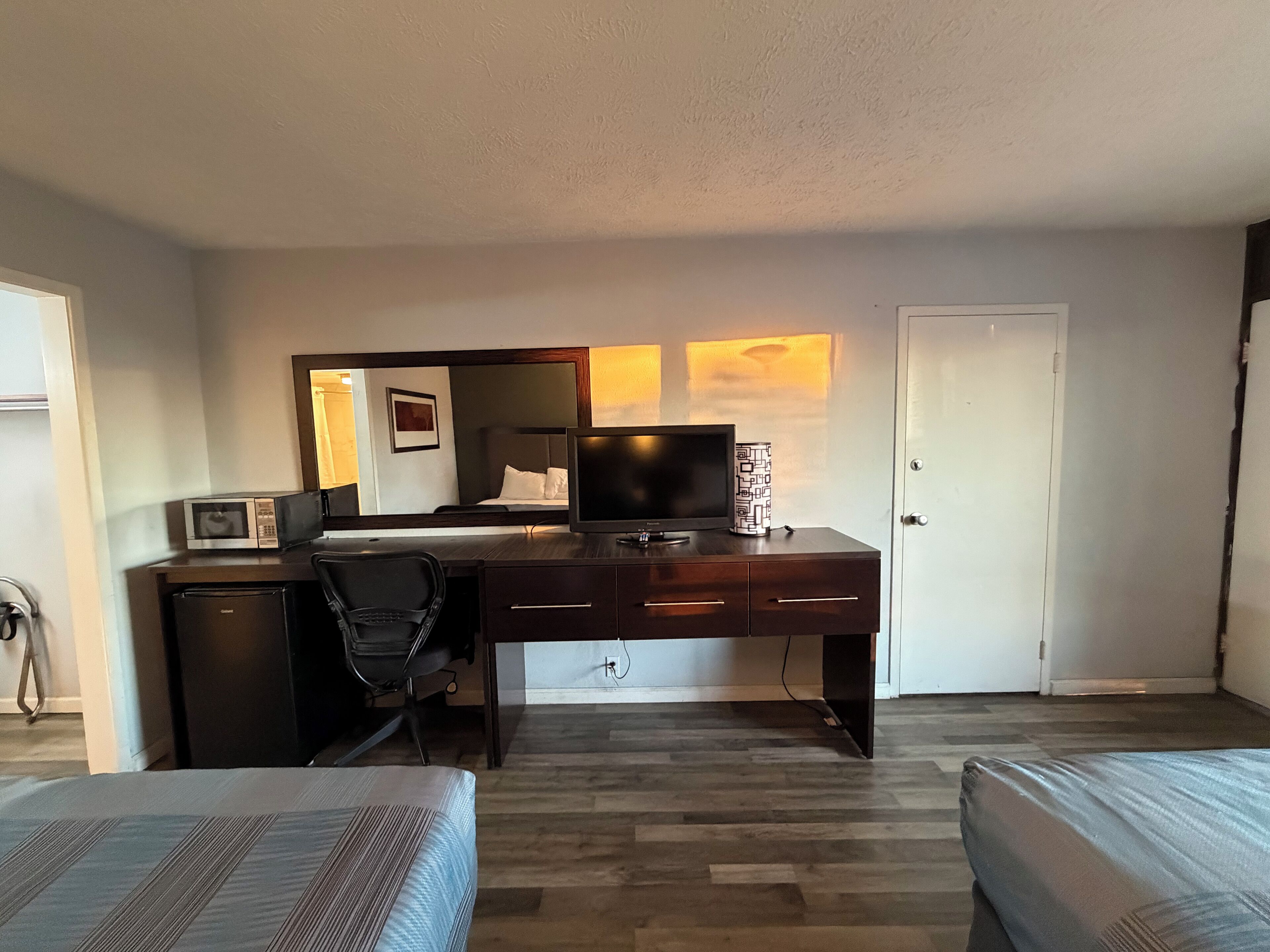 Habitación de hotel con un escritorio de madera, un televisor, un microondas, una silla y dos camas.