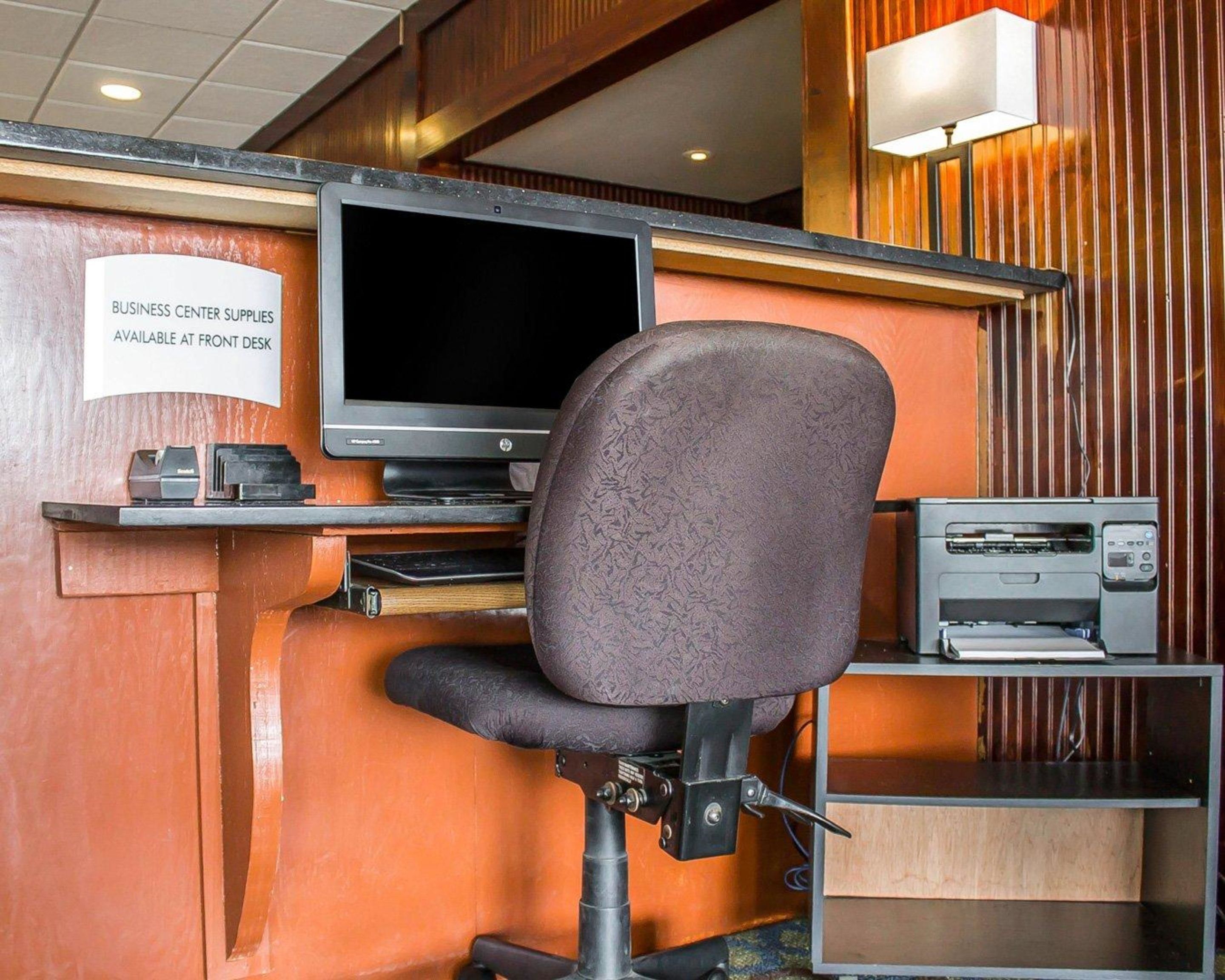 Un centro de negocios con computadora, impresora y un letrero que indica que hay útiles disponibles en la recepción.