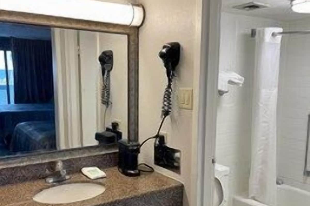 A bathroom with a sink, mirror, hairdryer, and toilet.