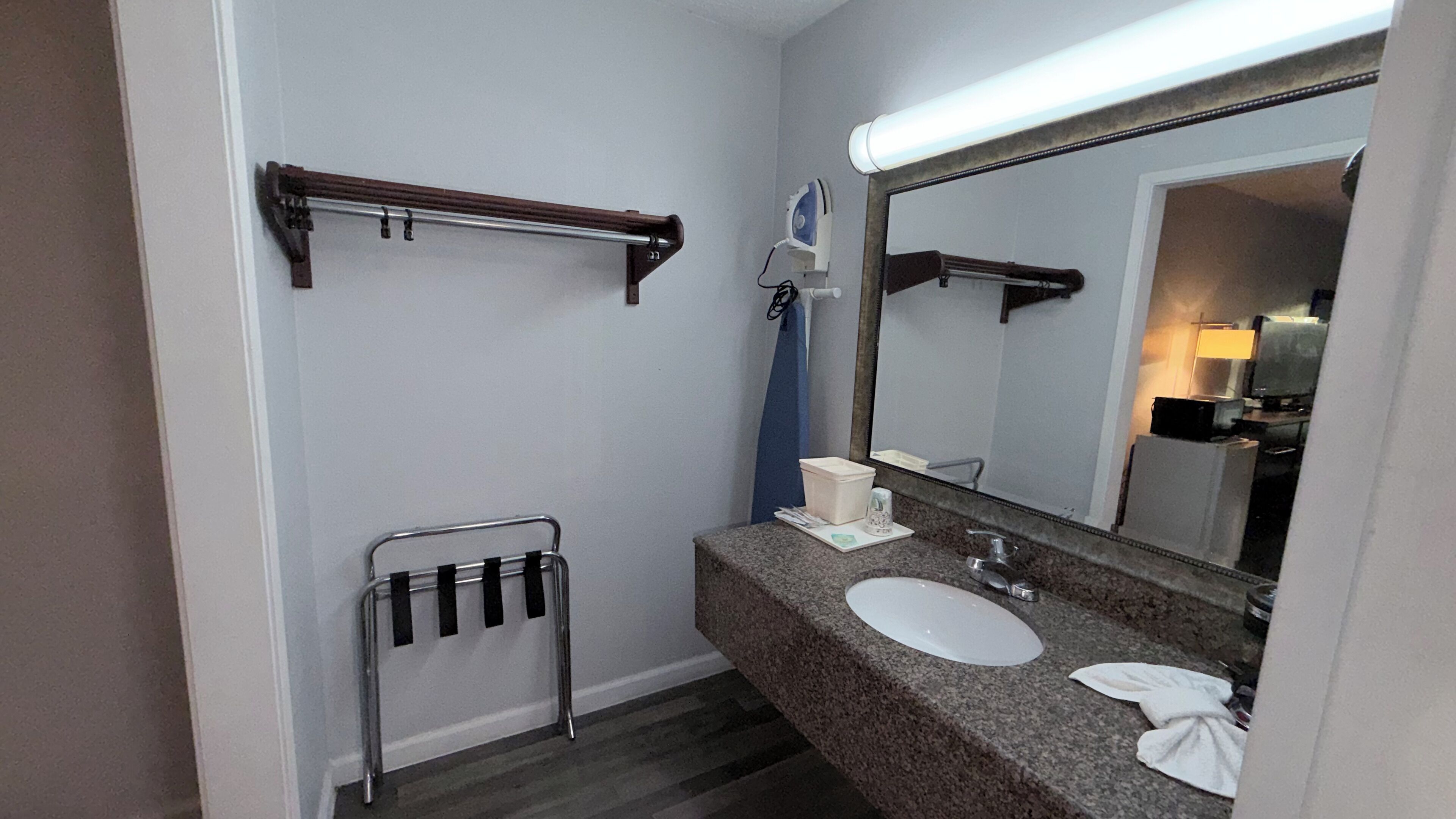 Un baño con encimera de granito, un lavabo, un espejo, un perchero para toallas y un secador de pelo.