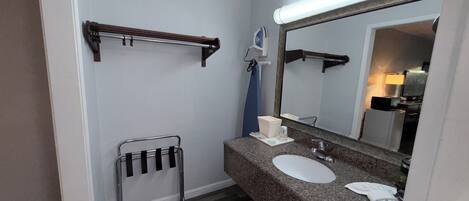 Un baño con encimera de granito, un lavabo, un espejo, un perchero para toallas y un secador de pelo.