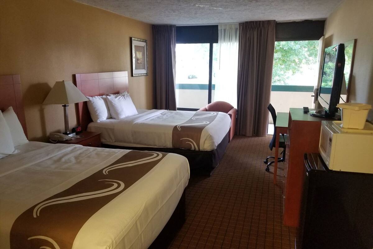 Ett hotellrum med två sängar, ett skrivbord, en stol, en tv och ett fönster med gardiner.